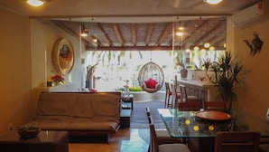 Un salon confortable avec un canapé, une table à manger, des chaises et un fauteuil suspendu. On peut admirer la verdure à travers la fenêtre.
