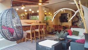 Un intérieur chaleureux avec un fauteuil suspendu, des chaises en bois, un coin bar et un espace détente avec des coussins.
