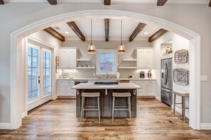 Une cuisine spacieuse avec un grand îlot central, des poutres en bois au plafond et des luminaires suspendus.