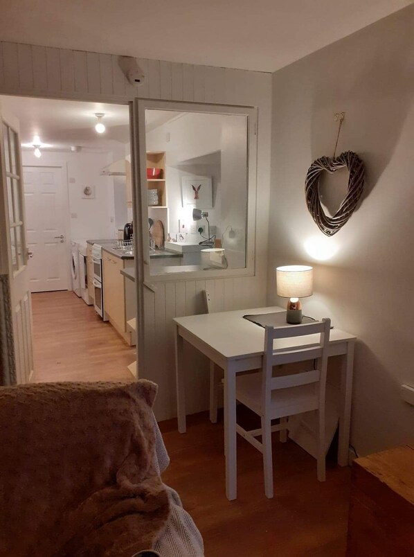 A compact kitchen with a dining area, a heart-shaped wall decoration, and a lamp on the table.