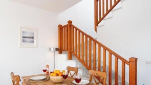 Ein Essbereich mit einer Holztreppe, einem gerahmten Bild an der Wand und einem Tisch, gedeckt mit Weingläsern, Tellern und einer Obstschale.