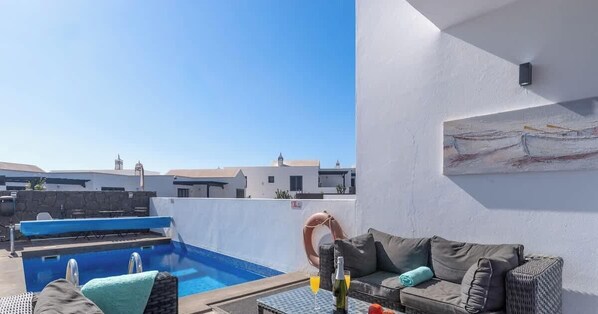 Un área de piscina en la azotea con una tumbona, una mesita con bebidas y un cuadro en la pared.