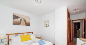 Un dormitorio con cama de madera, paredes blancas y un cuadro de un puente.