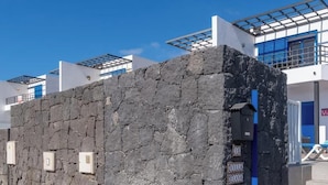 Eine Steinsäule mit einer blauen Tür, einem Metallgitter und einer Treppe, die zu einem Gebäude mit blauen Fenstern und einer weißen Fassade führt.
