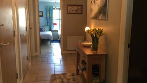 Un couloir avec une porte en bois, un radiateur, un vase de fleurs et un tableau accroché au mur.