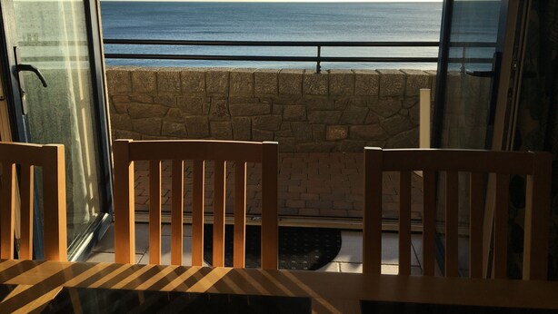 Un balcon avec vue sur la mer, des murs en pierre et des chaises en bois.