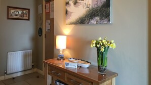 Un comptoir d’accueil avec une lampe, une pancarte de bienvenue, un tableau encadré et un vase de fleurs.