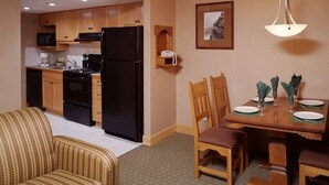 A compact kitchen with wooden cabinets, a black refrigerator, and a dining area with a wooden table and chairs. - Spacious two-bedroom fully outfitted condo in Banff (Banff)