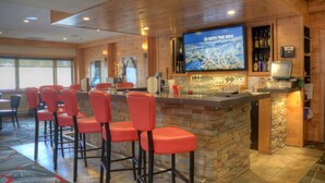 A bar area with a stone counter, red bar stools, a television screen, and a wooden interior. - Spacious two-bedroom fully outfitted condo in Banff (Banff)