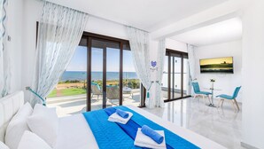Une chambre d’hôtel moderne dotée d’un grand lit, d’un balcon avec vue sur la mer et d’un coin repas avec des chaises et une table.