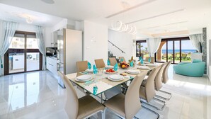 Un espace repas moderne avec une table en verre, des chaises de couleur beige et une vue sur la mer.