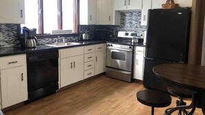 A kitchen with white cabinets, a black refrigerator, a stove, and a sink. - Nice 3 Bed Apt near Downtown Boston (Revere)