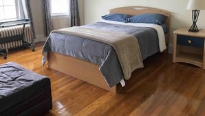 A bedroom with a bed, a bedside table, a lamp, and a radiator. - Nice 3 Bed Apt near Downtown Boston (Revere)