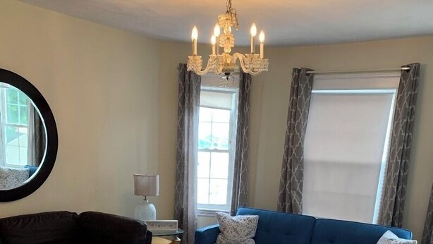 A living room with a blue sofa, a dark brown sofa, a patterned rug, a chandelier, and a window with curtains. - Nice 3 Bed Apt near Downtown Boston (Revere)