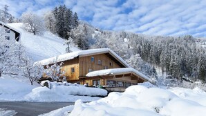 Una cabaña de madera con techo inclinado, rodeada de árboles cubiertos de nieve y un cielo despejado.