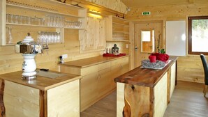 Interior de una cabaña de madera con una isla central, estantes con cristalería y una mesa de madera rústica.