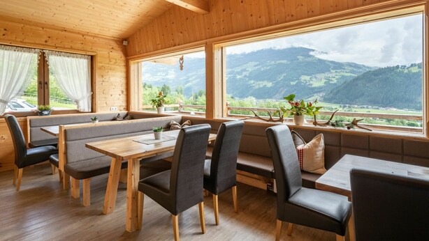Una cabaña de madera con comedor, ventanas amplias y vistas a montañas.