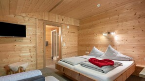 Dormitorio con paneles de madera, una cama, un televisor y zona de ducha.