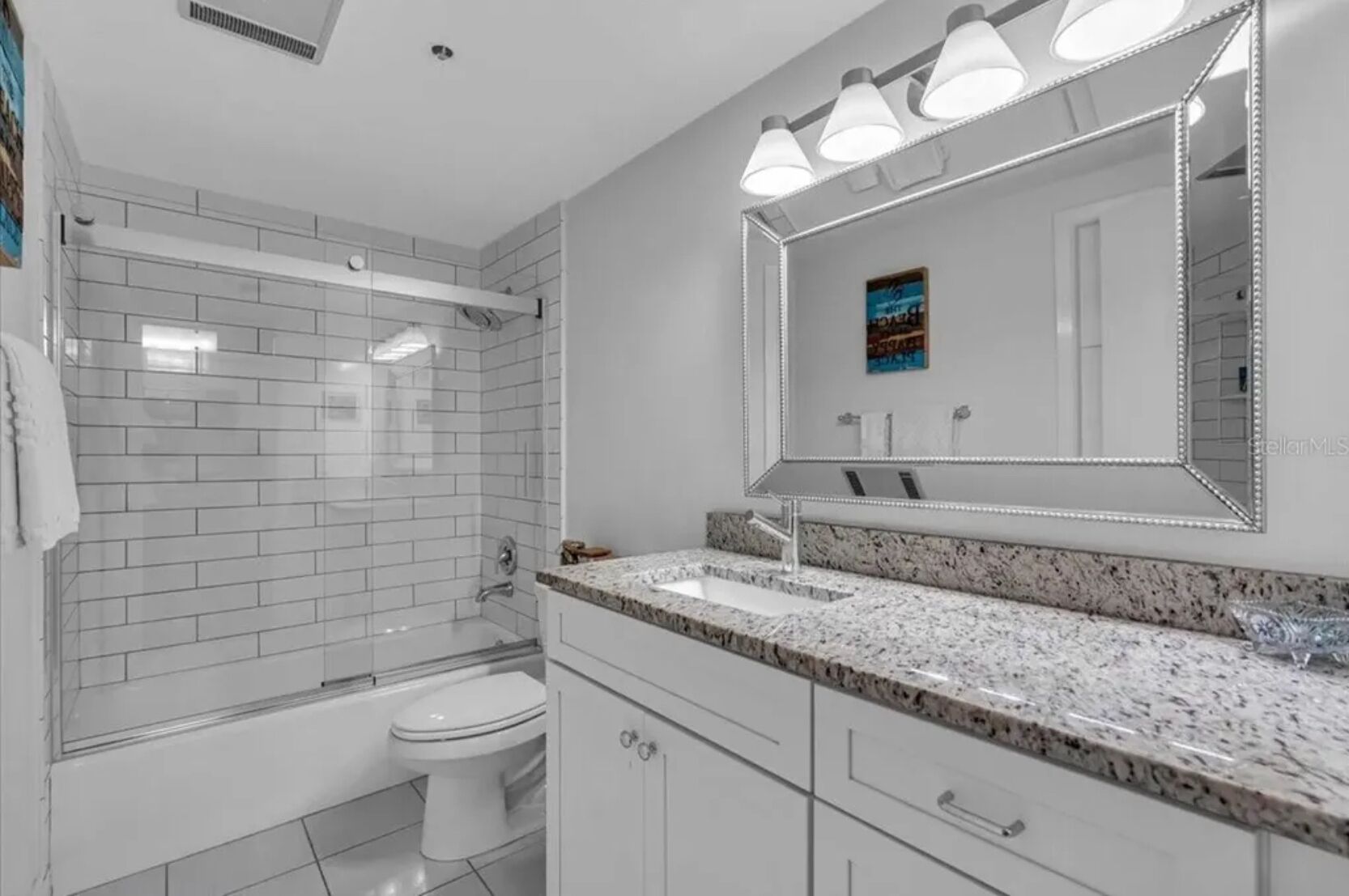 A modern bathroom with a glass shower enclosure, a white toilet, a granite countertop, and a large mirror with LED lights.
