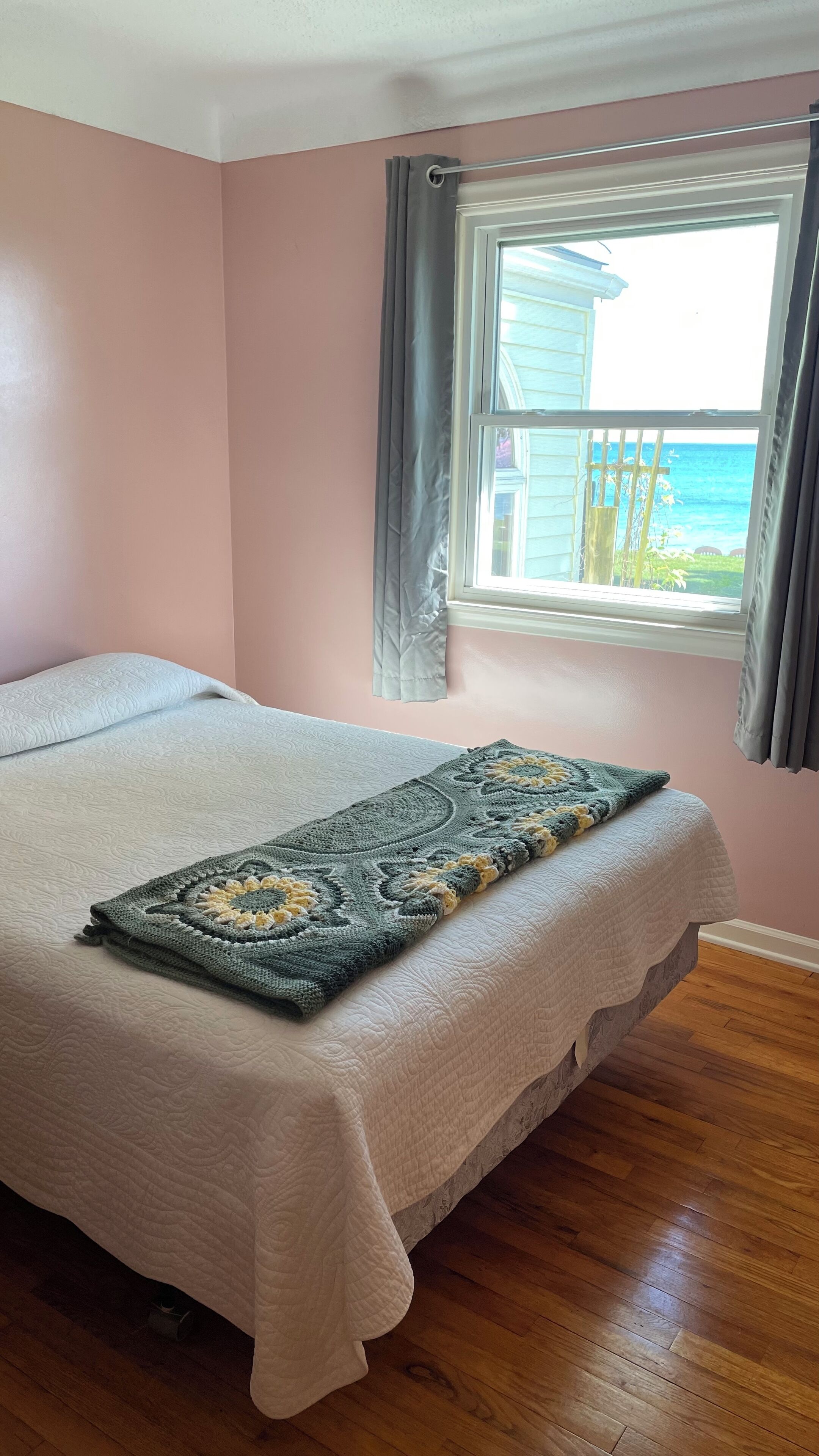 Un dormitorio con cama, ventana con cortinas y vista al océano.