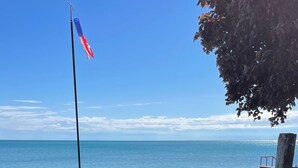 A grassy area with a flagpole, a stone pathway, and a view of the sea. - Lake Huron Beach  (Fort Gratiot Twp)
