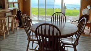 A dining area with a round table and chairs, large windows with a view of the ocean, and wooden walls. - Lake Huron Beach  (Fort Gratiot Twp)