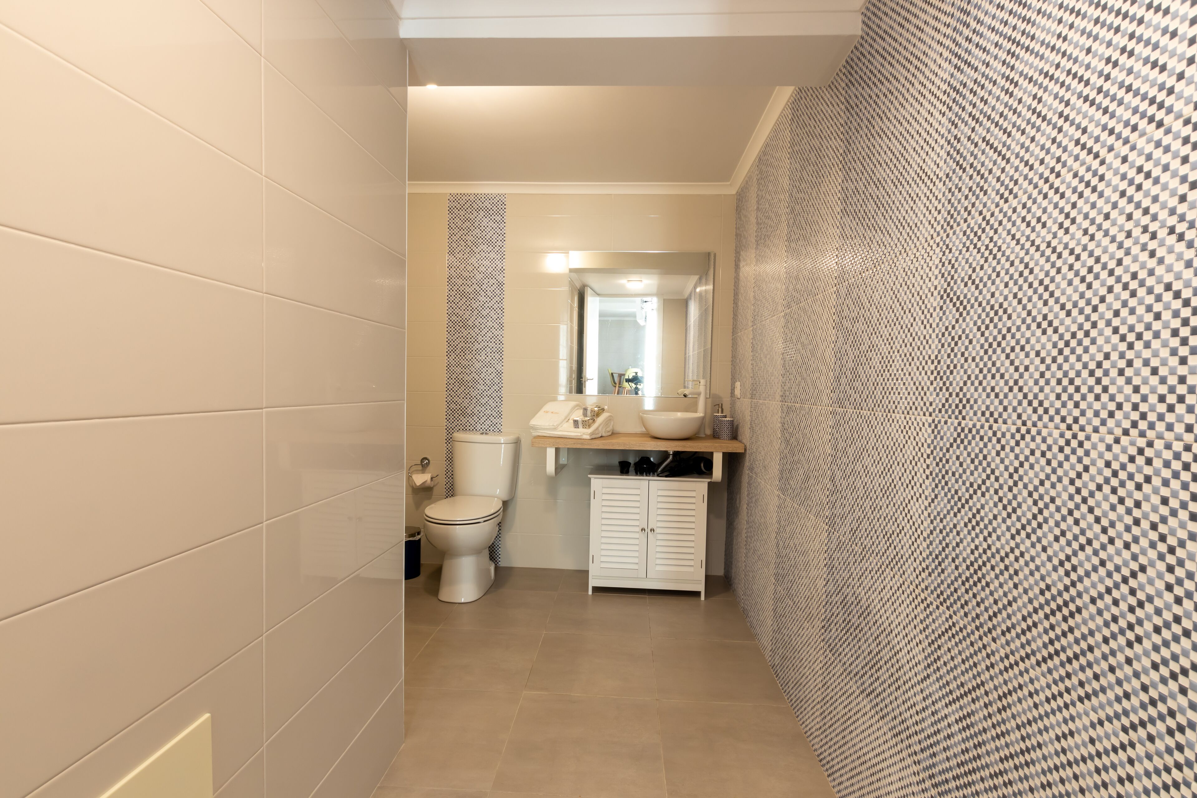 A narrow bathroom with a toilet, a sink with a mirror, and a cabinet.