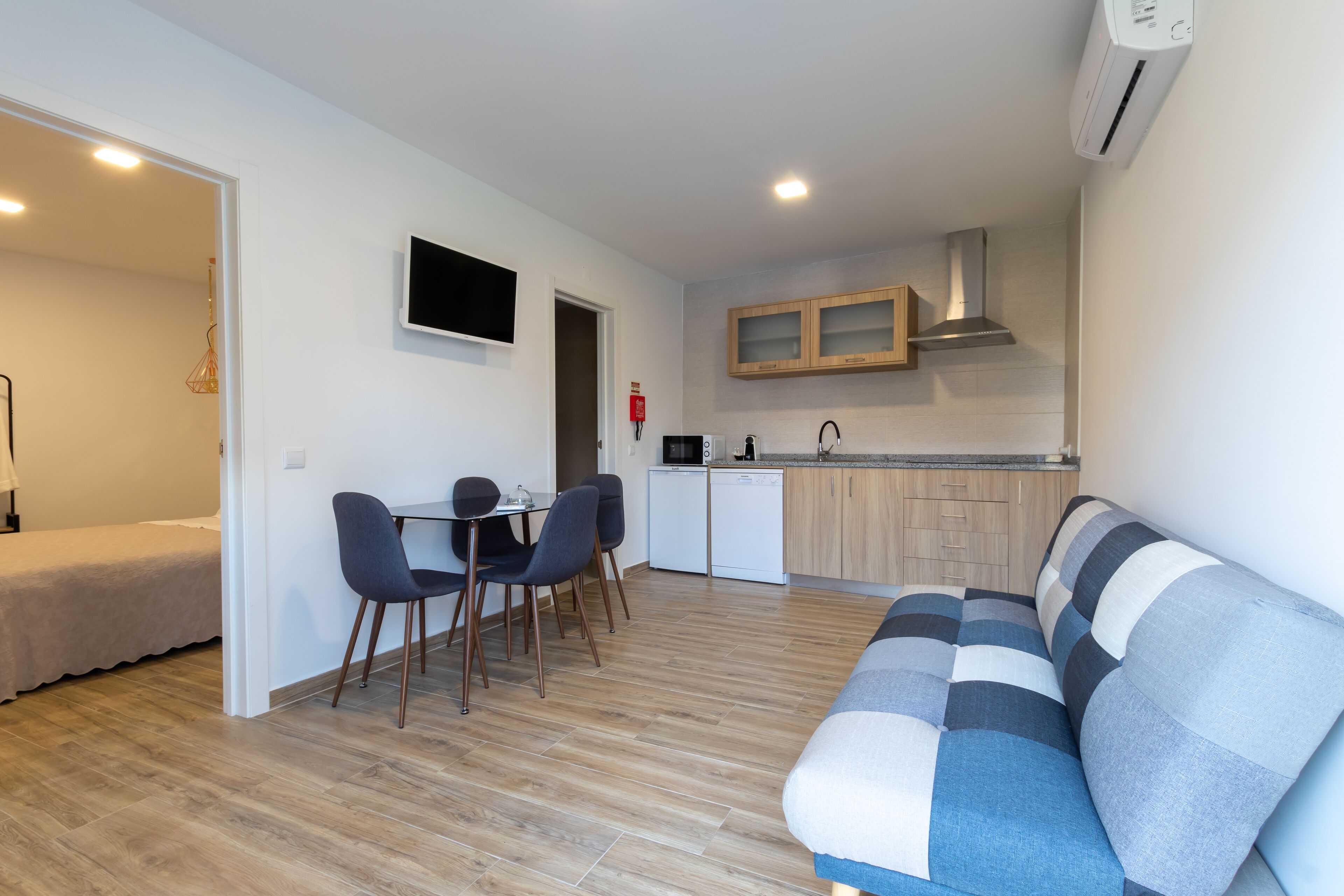 Una sala moderna con un sofá, un comedor con sillas, una cocina con armarios y un televisor montado en la pared.
