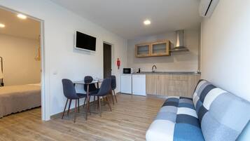 Una sala moderna con un sofá, un comedor con sillas, una cocina con armarios y un televisor montado en la pared.