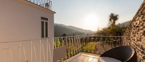 Un balcón con una silla de mimbre y vistas a un paisaje montañoso.