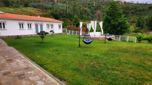 A white building with a red roof, a stone pathway, and a grassy lawn with hanging chairs. - Villa Alzira (Seia)