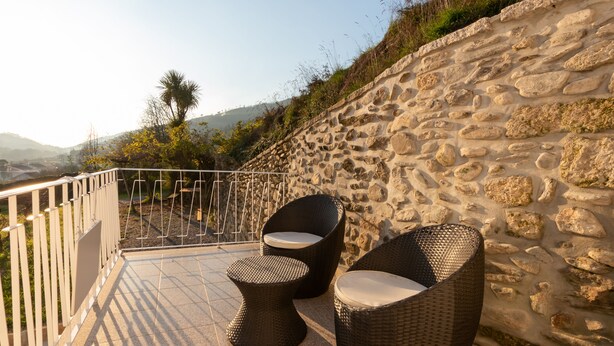 A terrace with wicker furniture, a stone wall, and a view of the landscape. - Villa Alzira (Seia)