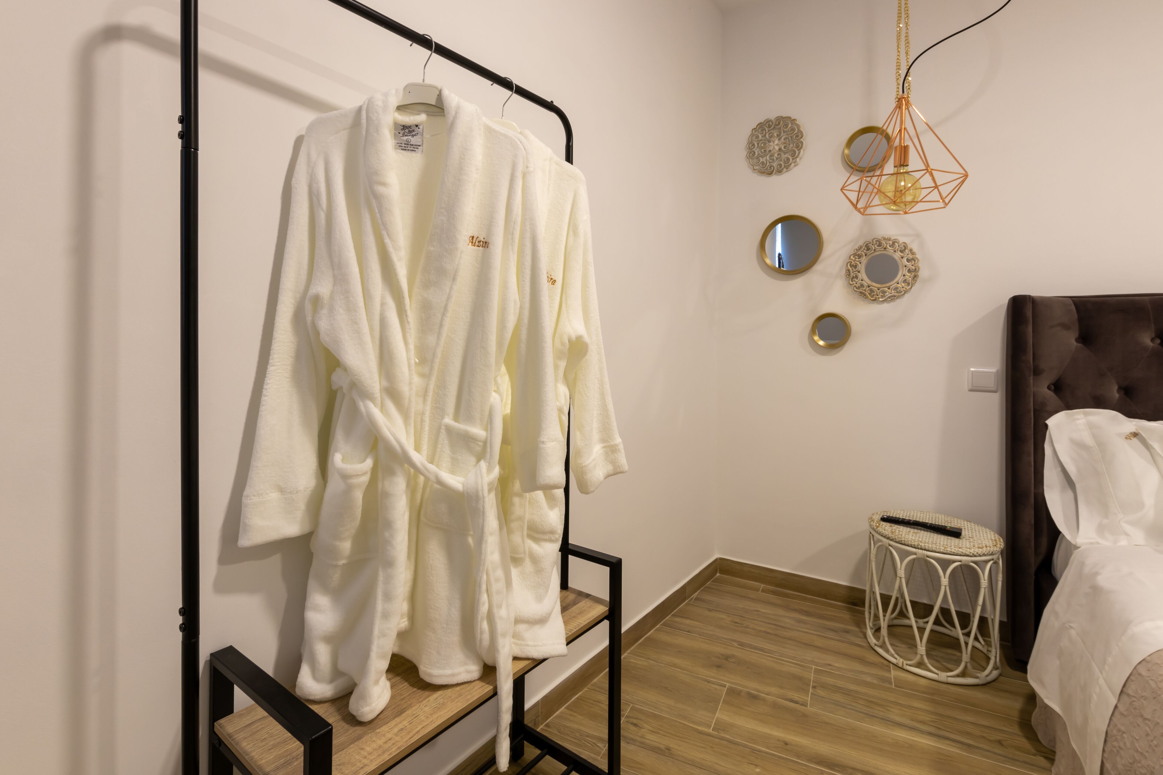 A hotel room with a wooden floor, a bed with white bedding, a white robe hanging on a rack, and decorative wall mirrors.