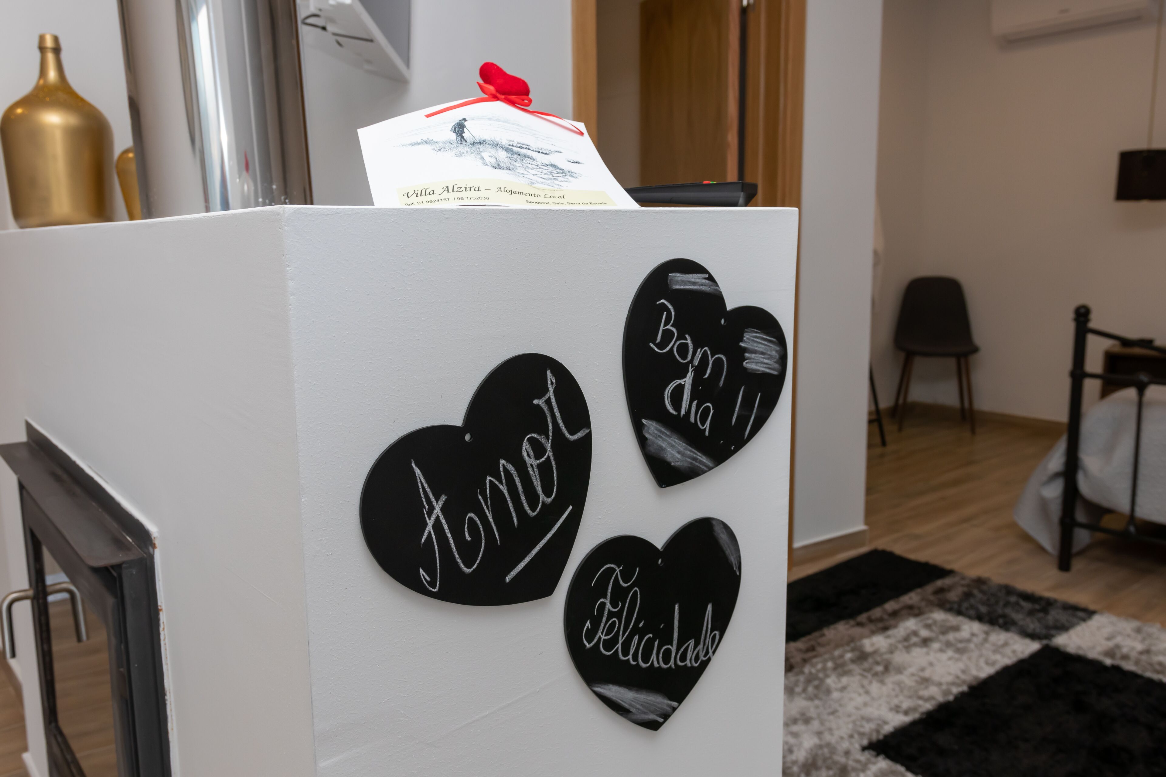 A room with a white reception desk, three black heart-shaped signs with names, a gold bottle, and a black and white rug.