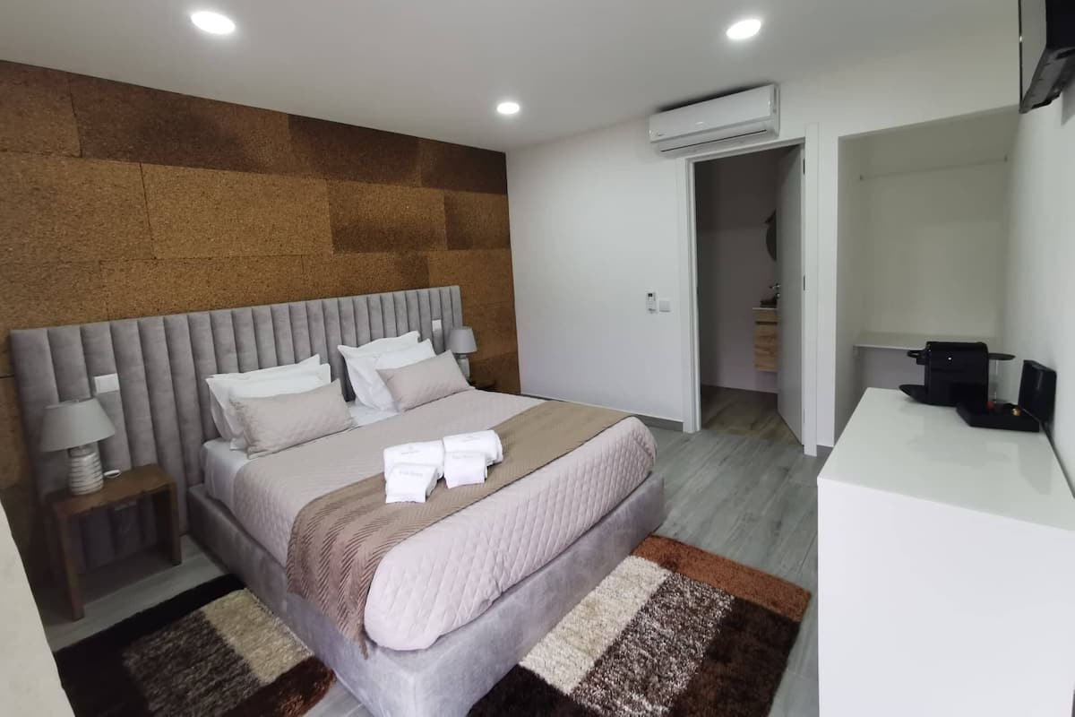 A modern bedroom with a large bed, bedside tables, an air conditioning unit, and a desk with a computer.