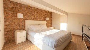 A bedroom with a stone wall, a bed with white bedding, a nightstand, and a bedside lamp. - Villa Alzira (Seia)