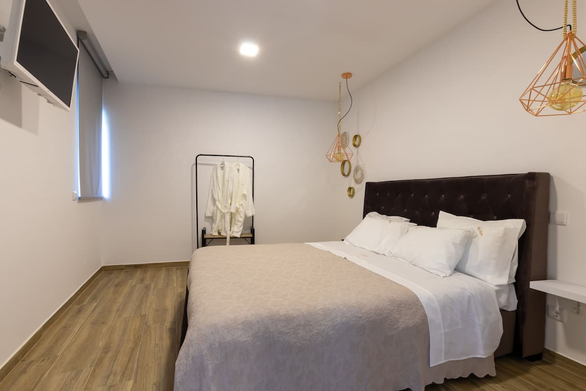 A bedroom with a large bed, a wardrobe, a hanging light fixture, and a window.