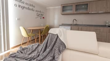 A modern kitchen with wooden cabinets, a dining area with a table and chairs, and a cozy living space with a sofa and a blanket.