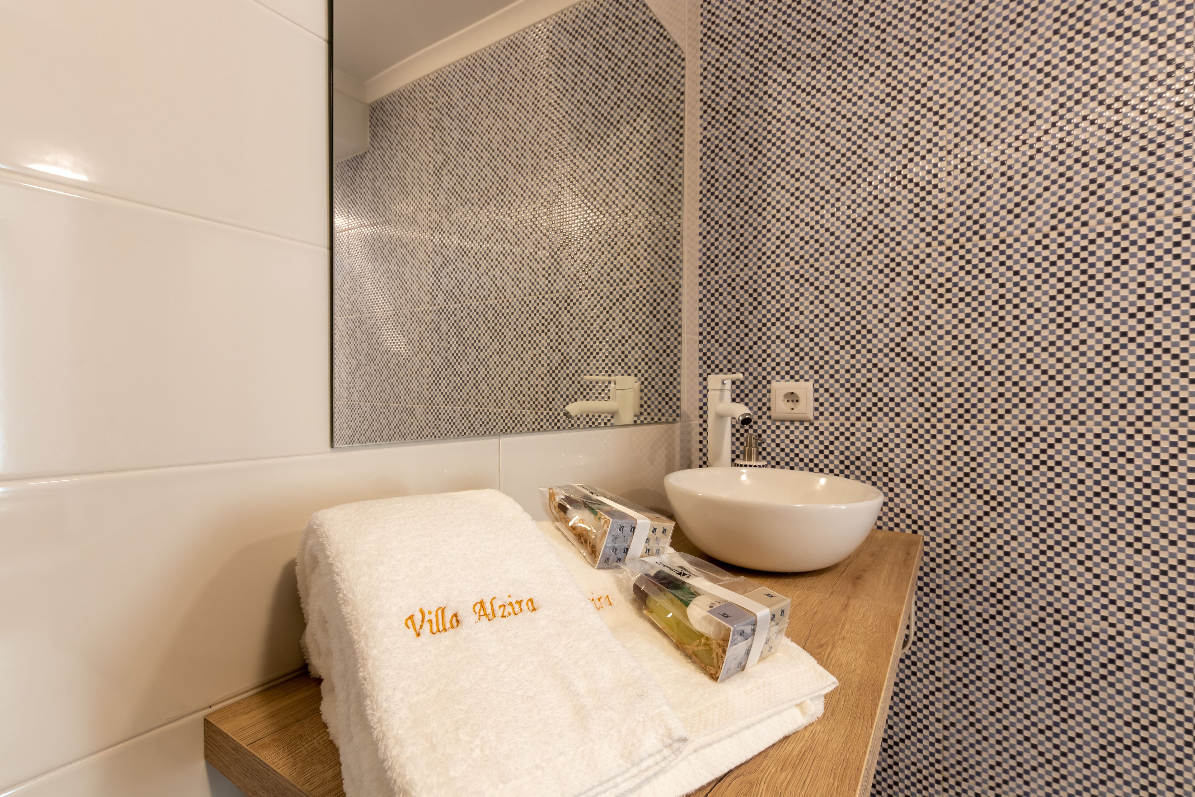 Un baño con lavamanos blanco, un espejo y una toalla con la inscripción 'Villa Azira'.
