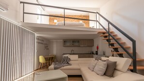 A modern living room with a sofa, a glass coffee table, a dining area with chairs, a kitchen with a sink, and a staircase. - Villa Alzira (Seia)