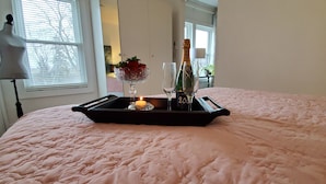A bed with a tray containing a candle, a glass, and a bottle of champagne.