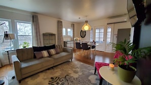 A living room with a sofa, a dining table with chairs, a chandelier, and a potted plant.