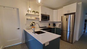 A modern kitchen with white cabinets, a stainless steel refrigerator, a microwave, and a sink with a faucet.