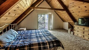 A bedroom with a sloped ceiling, a bed with a plaid bedspread, a dresser, and a television on top. - Jessup`s Cabin (Groveland)