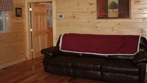 A wooden cabin interior with a leather sofa, a door, and a painting on the wall. - Hocking hills backwoods retreat -Whispering Winds (Rockbridge)