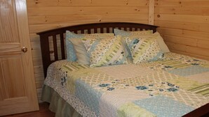 A wooden-paneled room with a bed featuring a quilted bedspread and multiple pillows. - Hocking hills backwoods retreat -Whispering Winds (Rockbridge)