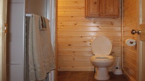 A small, wooden-paneled bathroom with a toilet, a towel hanging on the wall, and a wooden cabinet above the toilet. - Hocking hills backwoods retreat -Whispering Winds (Rockbridge)