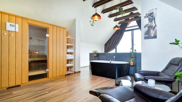 A modern living room with a black leather sofa, wooden flooring, a glass coffee table, a black bathtub, and a wooden wardrobe with glass doors.