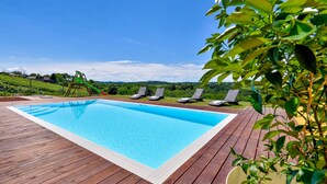A rectangular swimming pool with a wooden deck, surrounded by lounge chairs and a green slide.