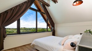 A bedroom with a large window, a bed, a bedside table, and a lamp.